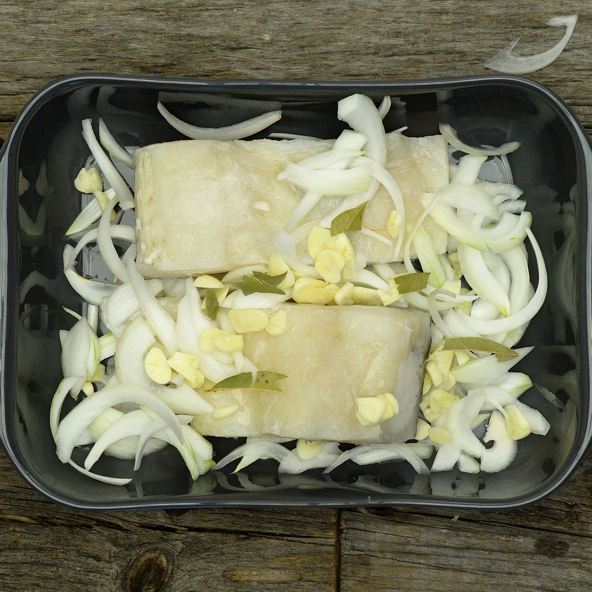 Lombos de bacalhau com alho fatiado, cebola e folhas de louro distribuídos por cima