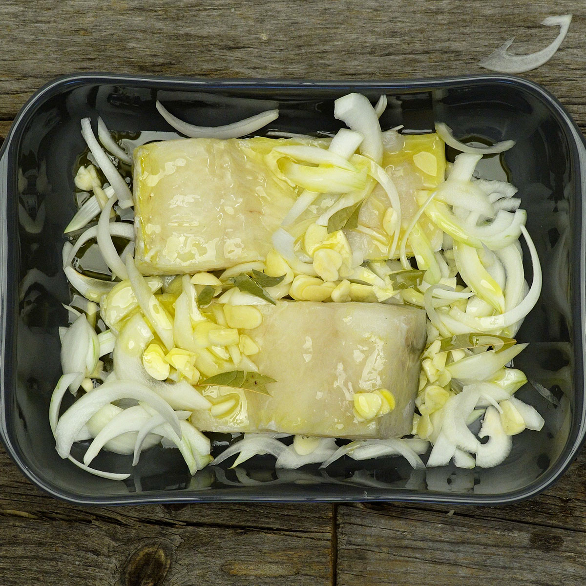 Travessa com bacalhau temperado e coberto com azeite, pronta para receber as batatas