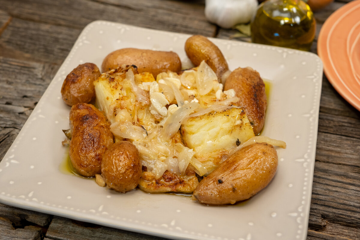 Ingredientes do bacalhau no forno com batatas dispostos na bancada: lombos, batatas, cebola, alho e azeite