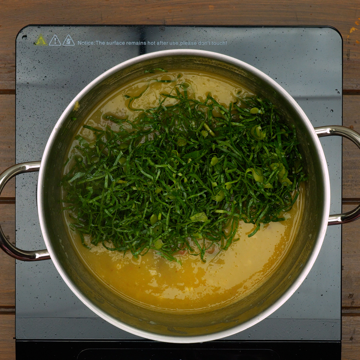 Couve finamente cortada sendo cozida no caldo até ficar macia e verde vibrante.