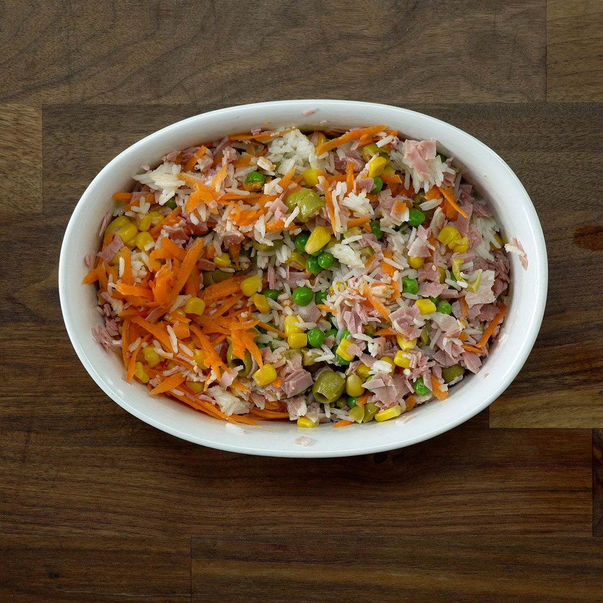 Arroz cozido misturado com legumes, bacon e presunto em uma travessa.