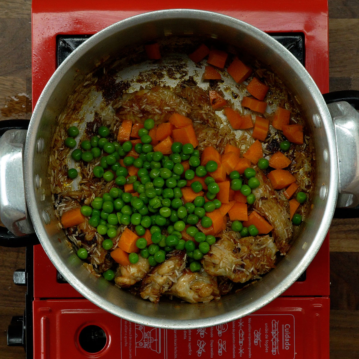 Arroz e legumes sendo adicionados à panela com frango.