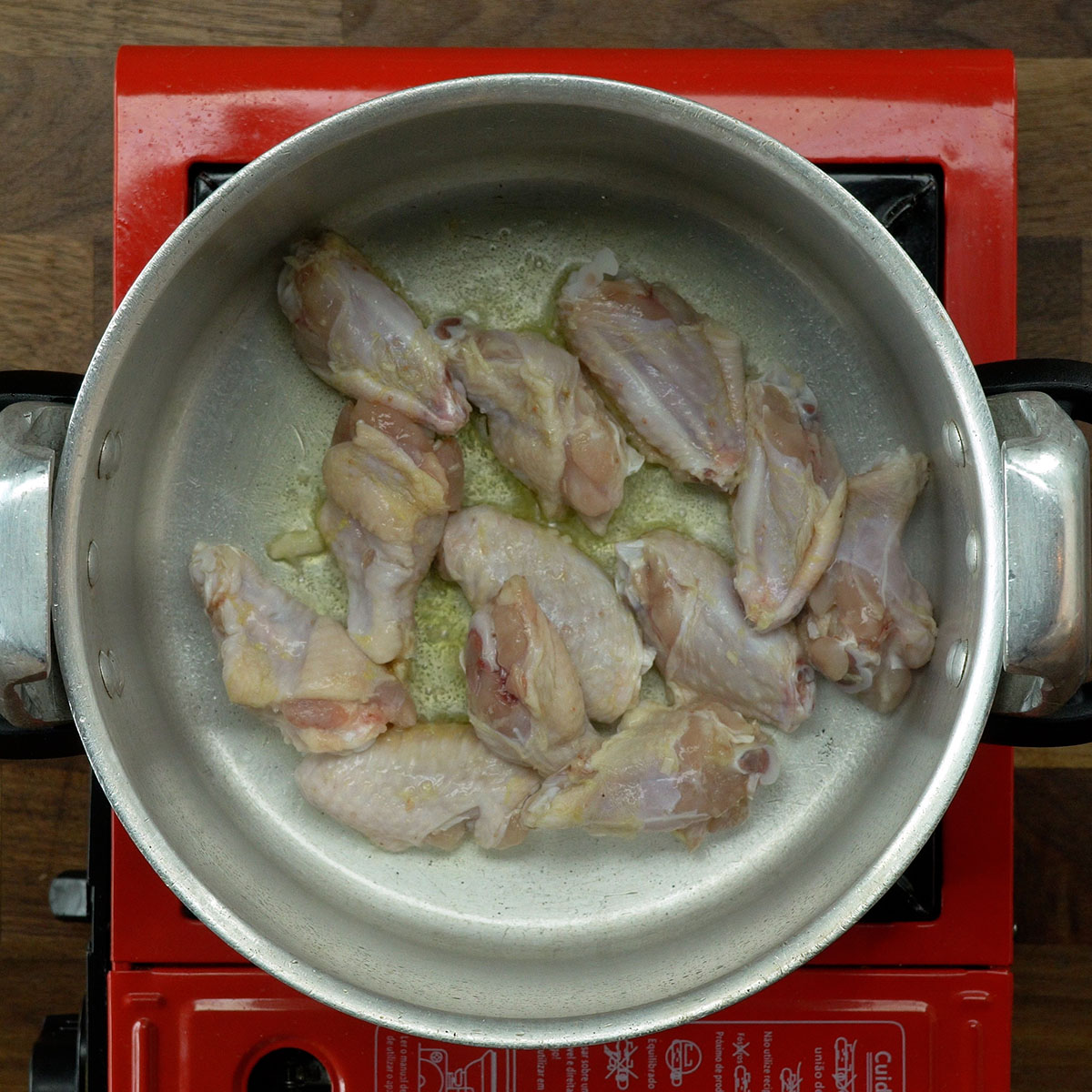 Asinhas de frango dourando na panela de pressão com azeite.