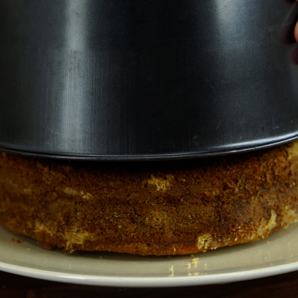 Bolo de maçã com canela sendo desenformado ainda morno sobre prato.