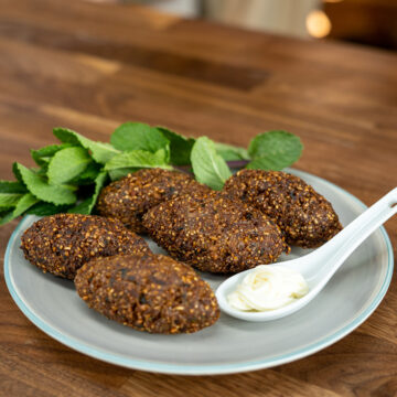 Empratamento kibes com molho de acompanhamento e hortelã de decoração.