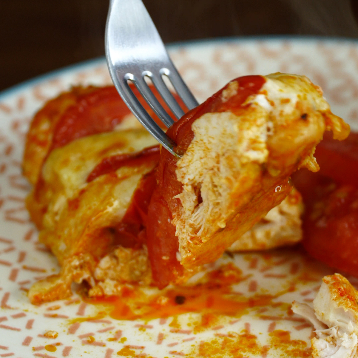 Peitos de frango recheados com tomate e muçarela espetados com um garfo.