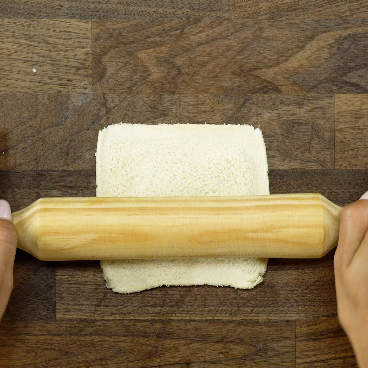 Fatias de pão de forma sendo abertas com rolo sobre a bancada.