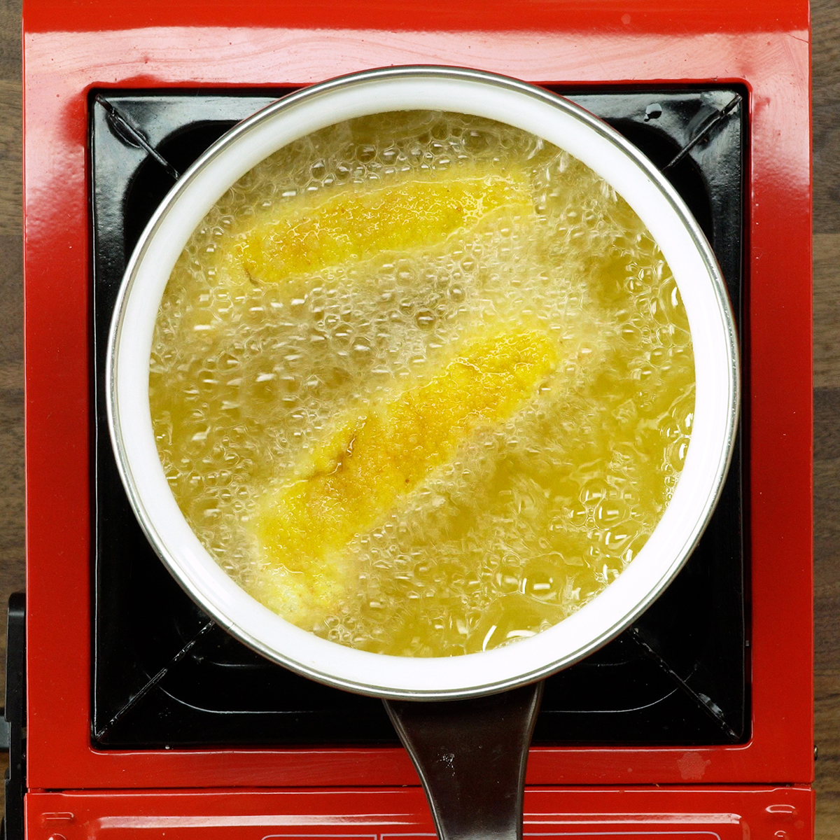 Enroladinho de pão de forma fritando em óleo quente até dourar.
