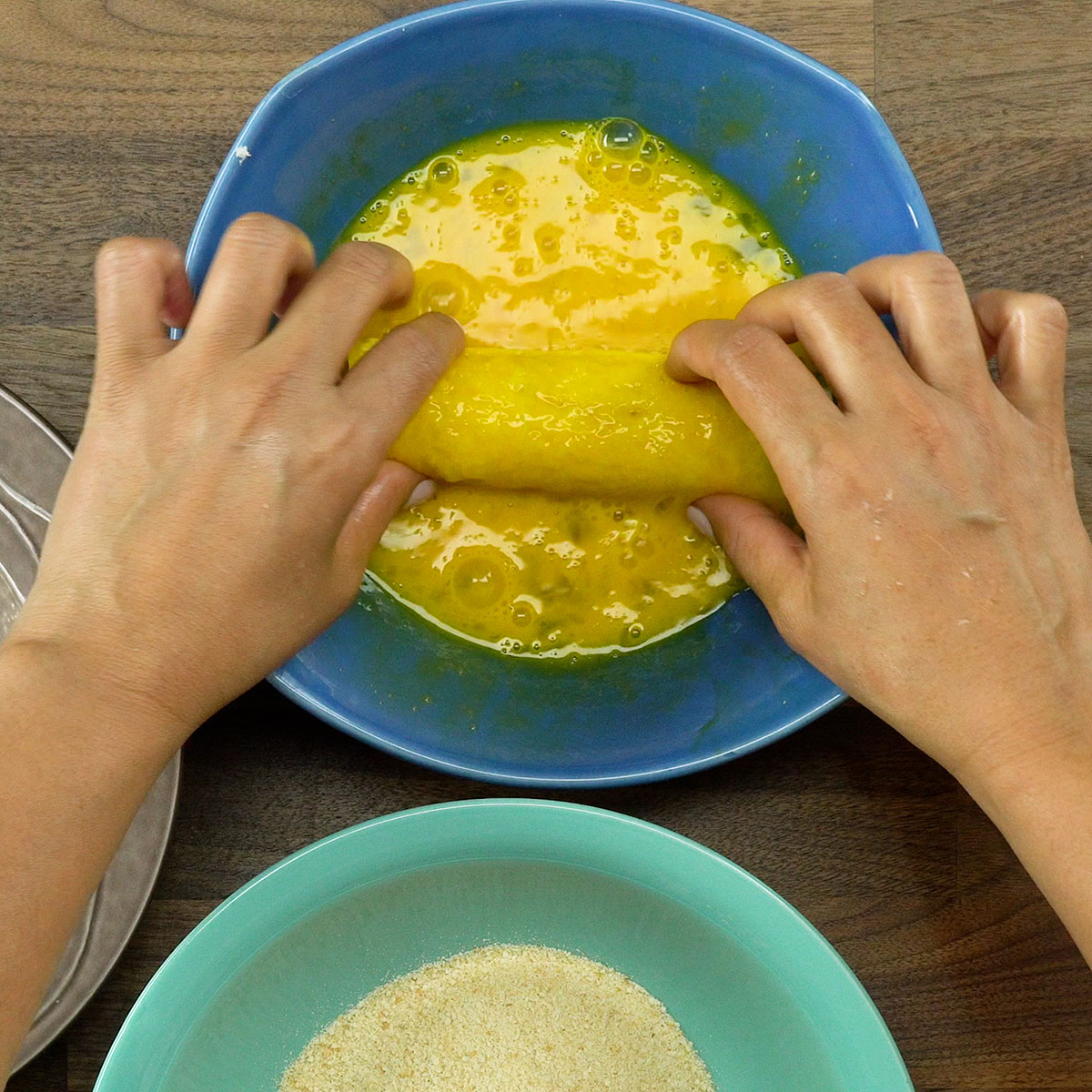 Enroladinho sendo mergulhado em ovo batido para empanar.