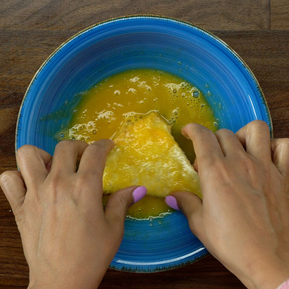 Pastel de pão de forma sendo mergulhado no ovo batido.