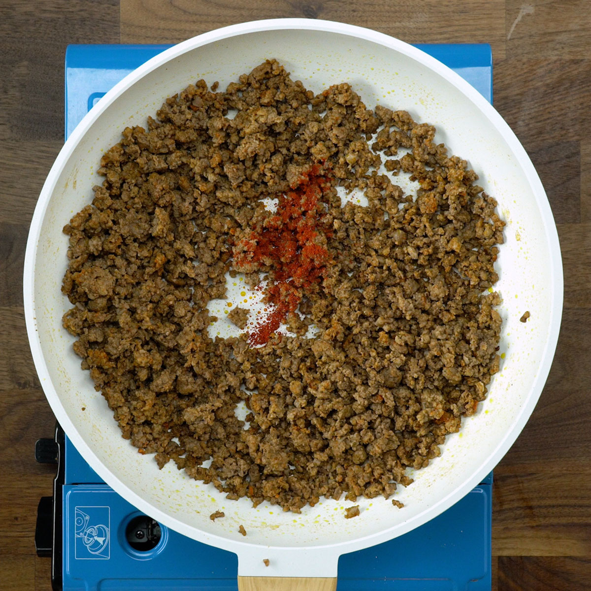 Carne moída sendo temperada com sal, pimenta-do-reino e colorau na frigideira.