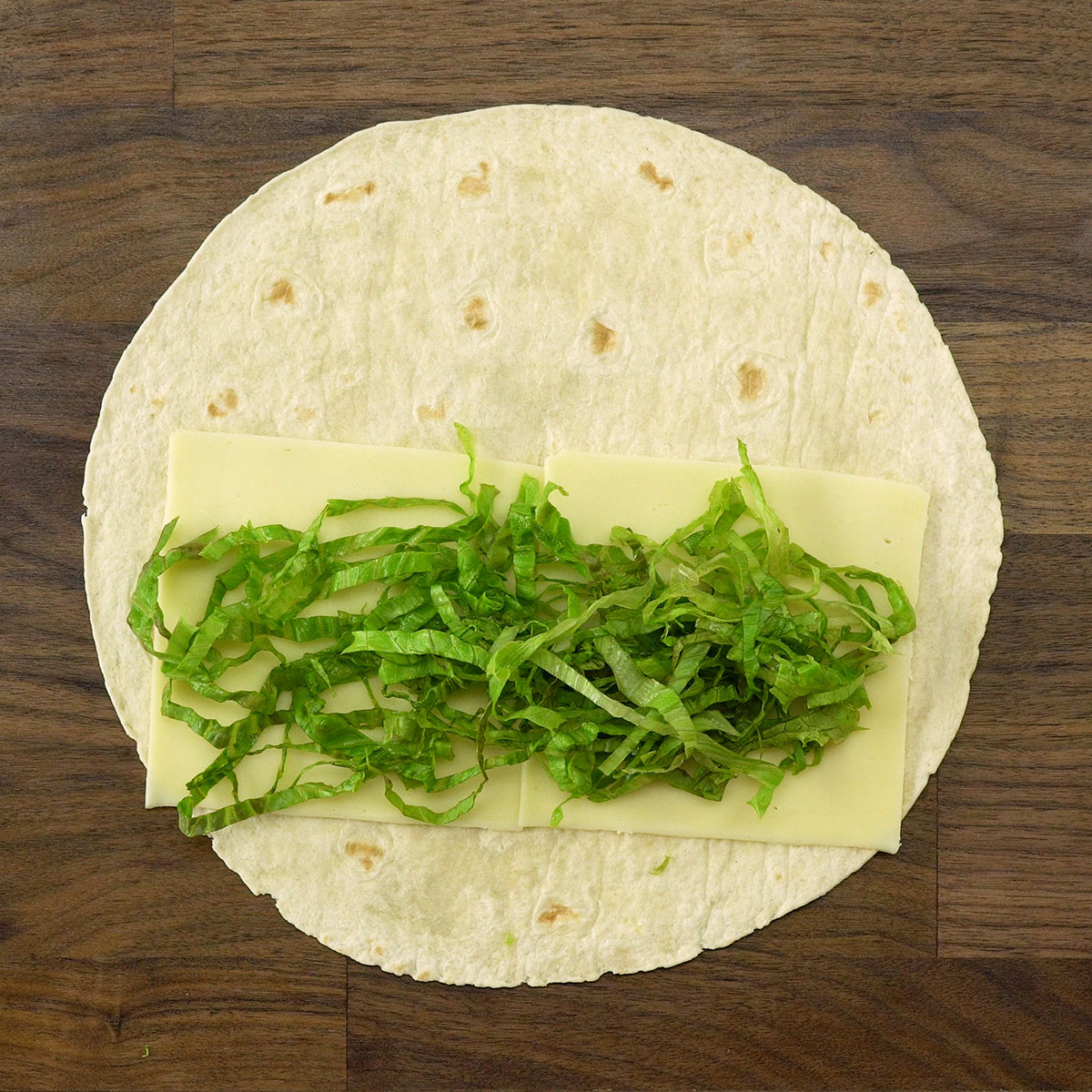 Alface fatiada sendo colocada sobre a massa do wrap.