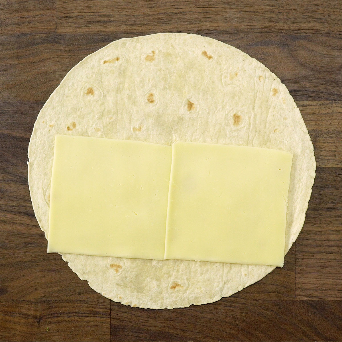 Fatias de muçarela sendo colocadas sobre a massa do wrap.