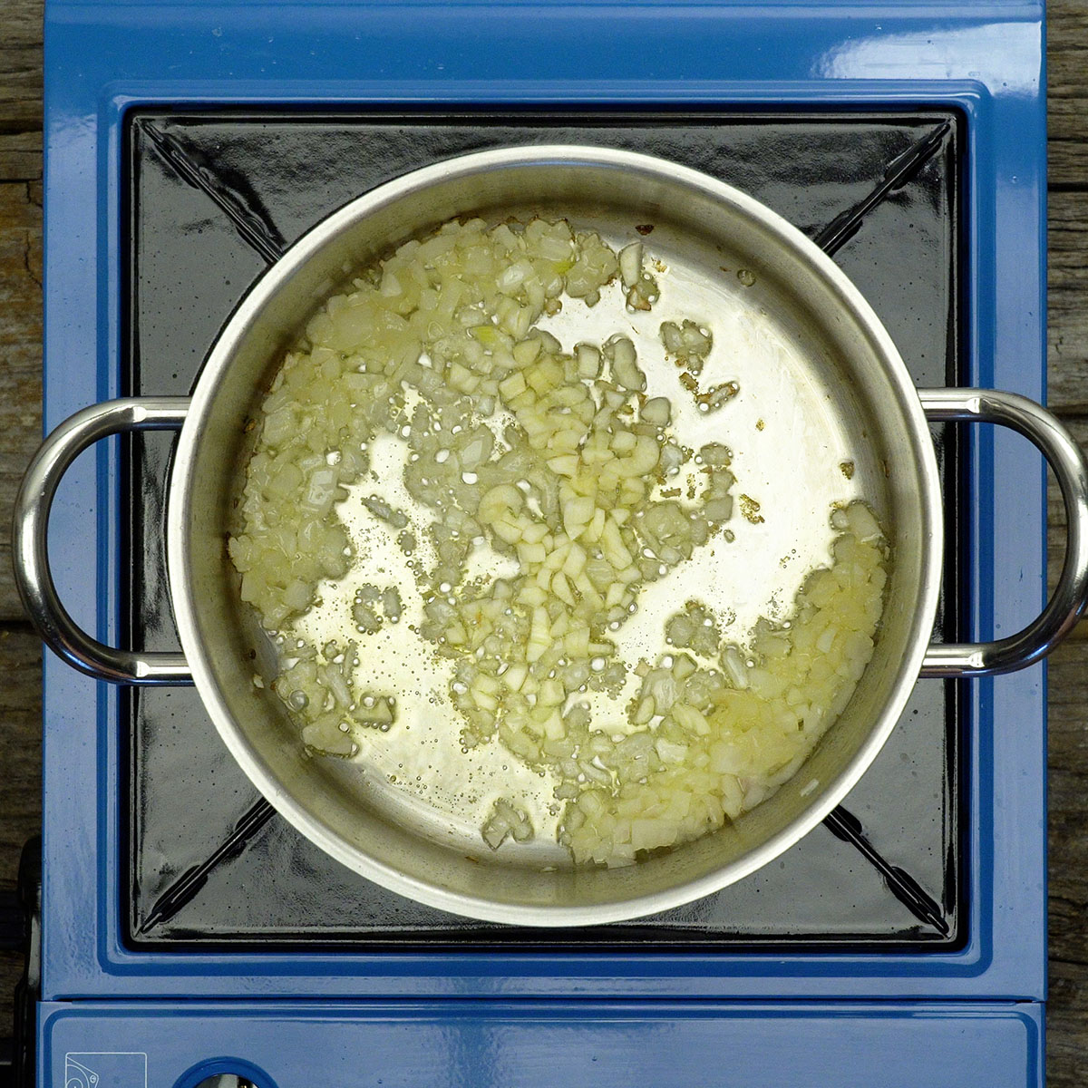 Cebola e alho sendo refogados em panela com azeite.