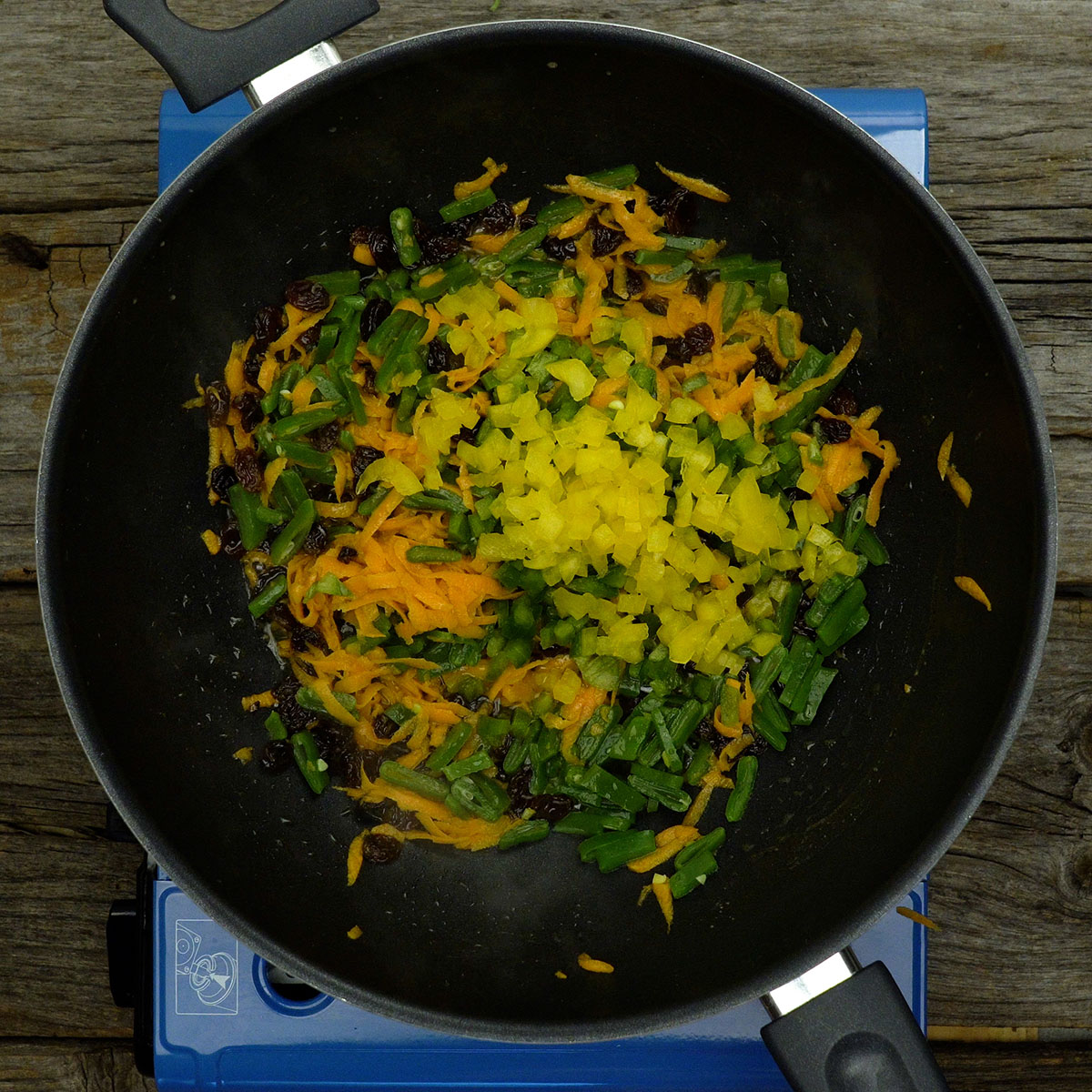 Legumes coloridos e uvas-passas sendo refogados.