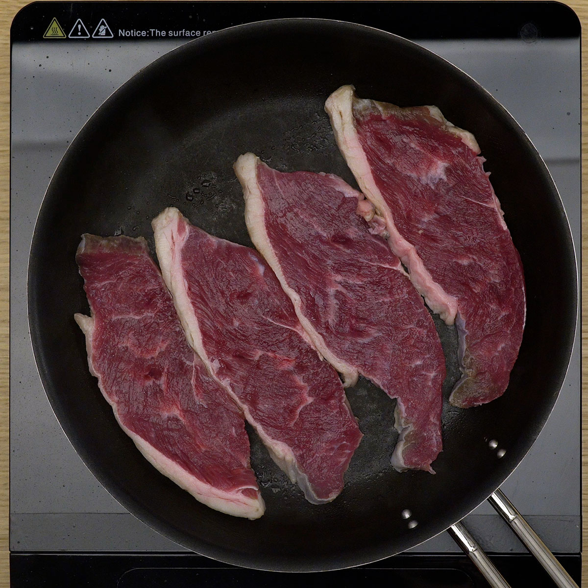 Bifes de contrafilé sendo grelhados na frigideira com azeite até dourar.
