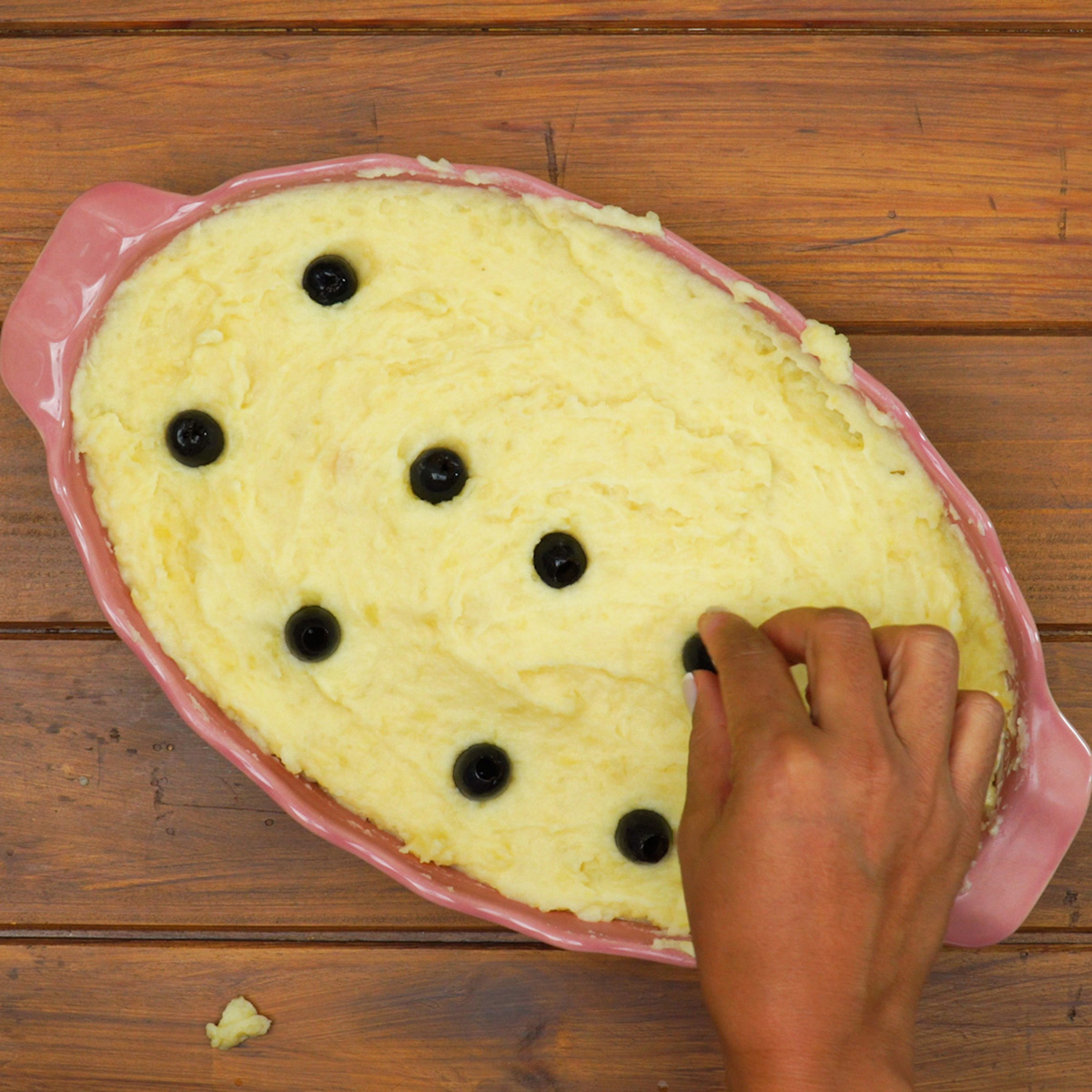 Montagem do Bacalhau à Zé do Pipo em travessa com camadas de purê e bacalhau.