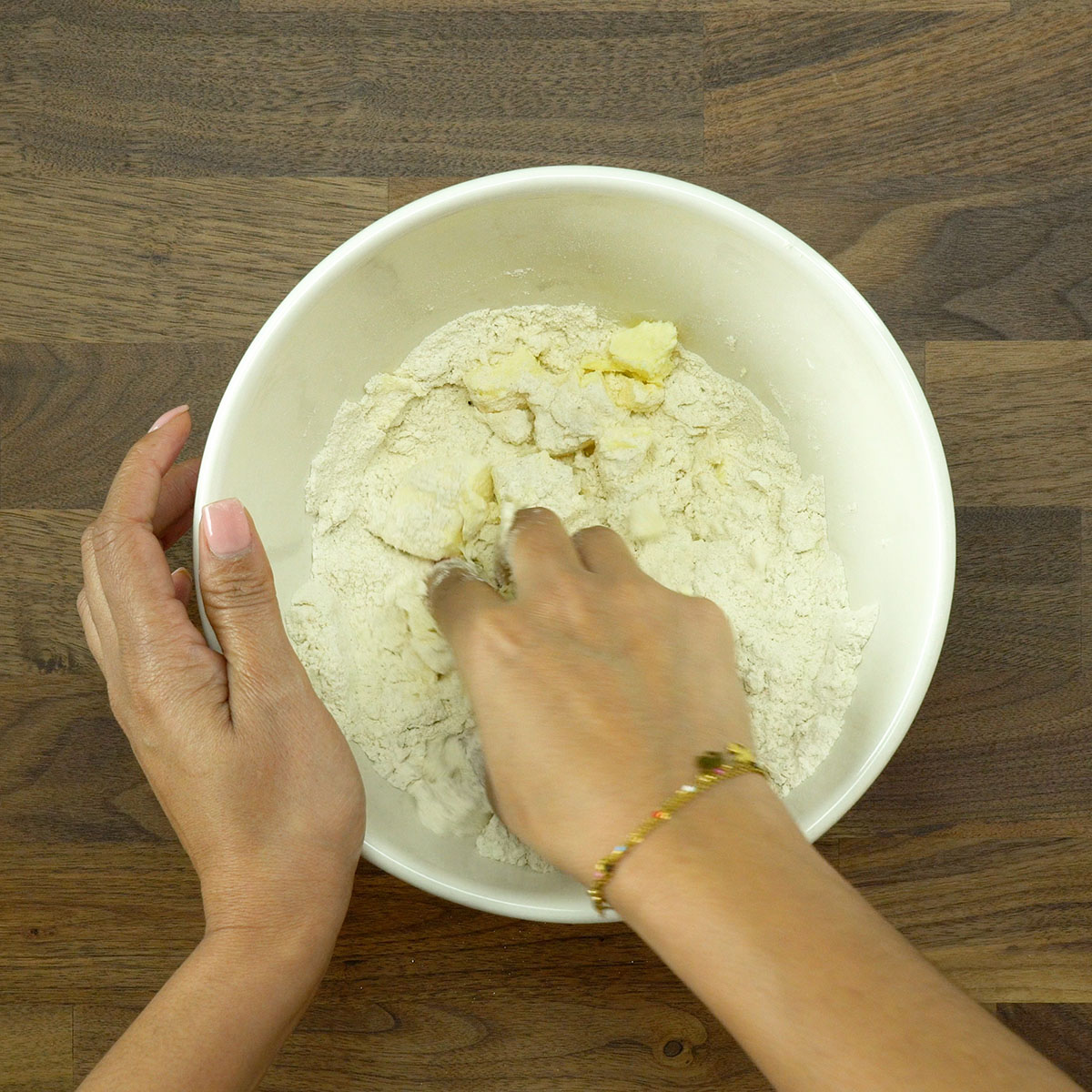 Mãos misturando a manteiga à farinha para formar a massa do biscoito salgado.