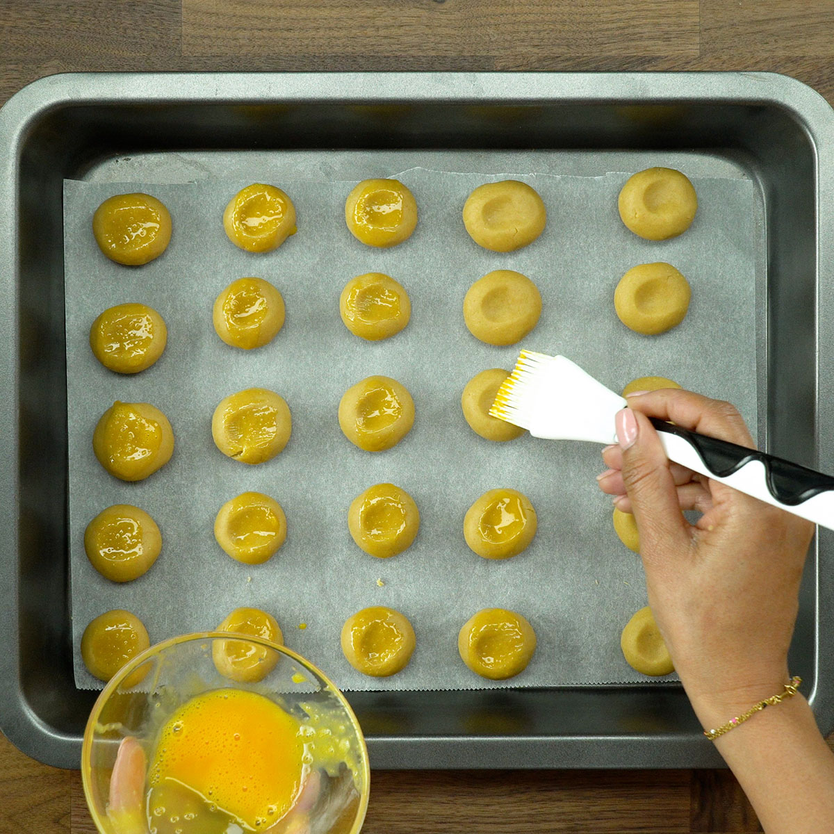 Biscoitos salgados sendo pincelados com gema de ovo antes de assar.