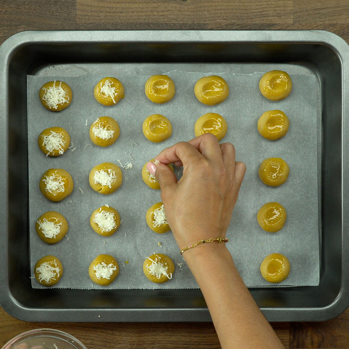Queijo parmesão ralado sendo salpicado sobre biscoitos crus.