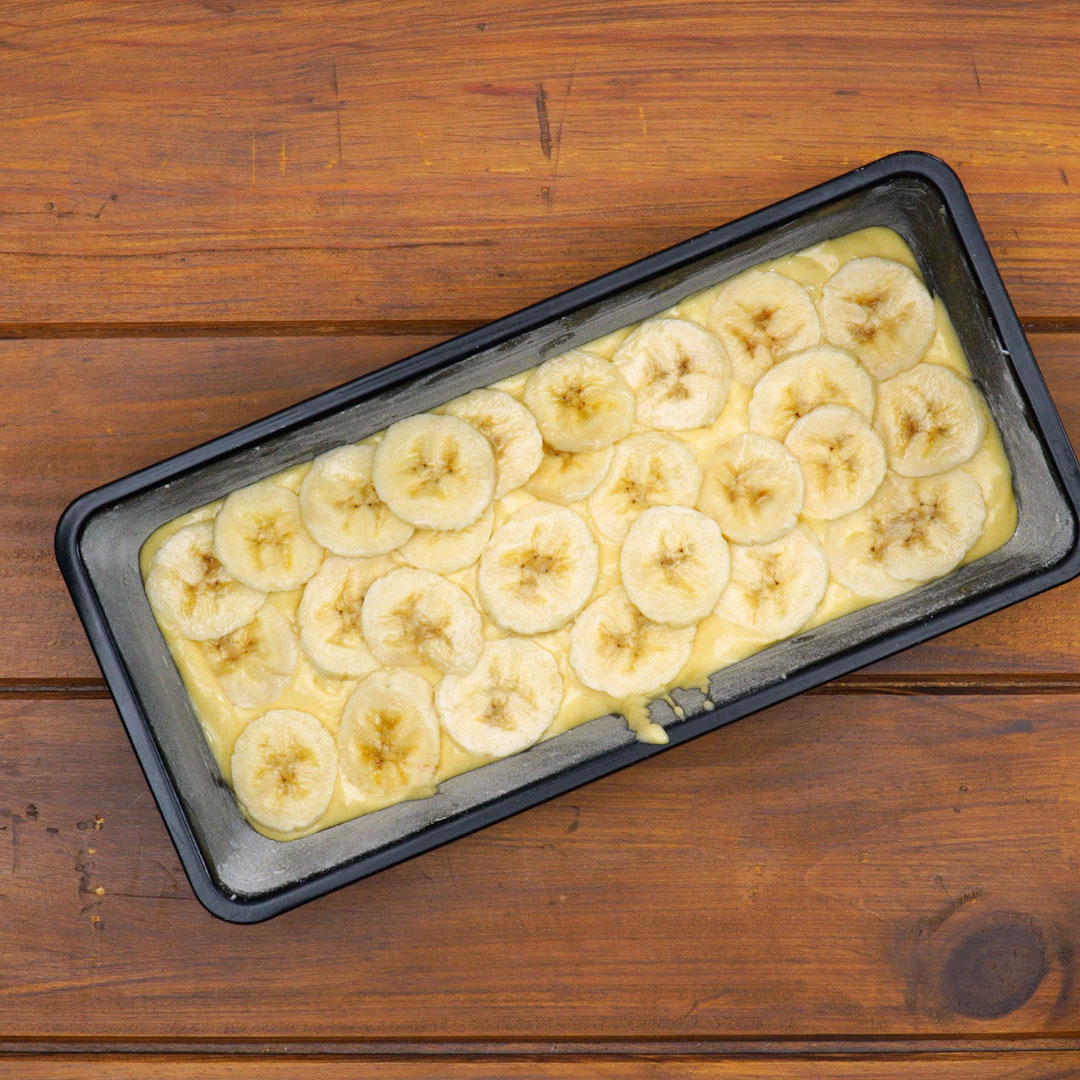 Montagem do bolo de banana na forma com camadas de massa e rodelas.