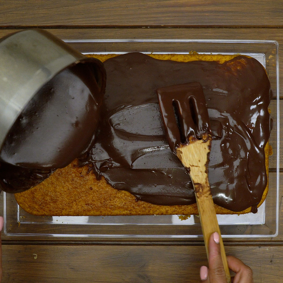 Cobertura de chocolate sendo espalhada sobre o bolo de cenoura desenformado.
