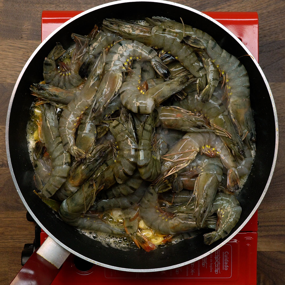 Camarões sendo adicionados à frigideira com alho dourado.