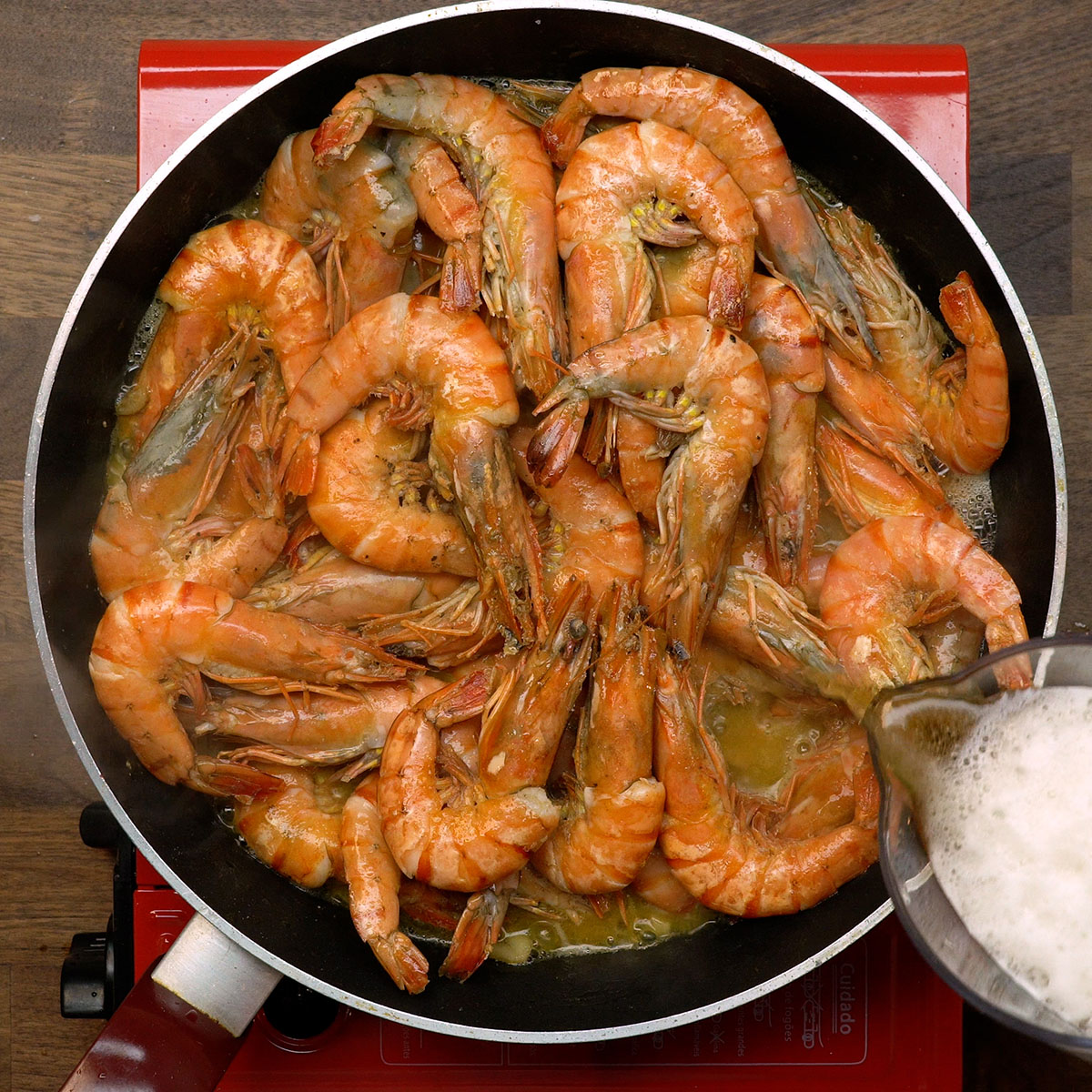 Cerveja sendo adicionada ao camarão para formar um molho suculento.