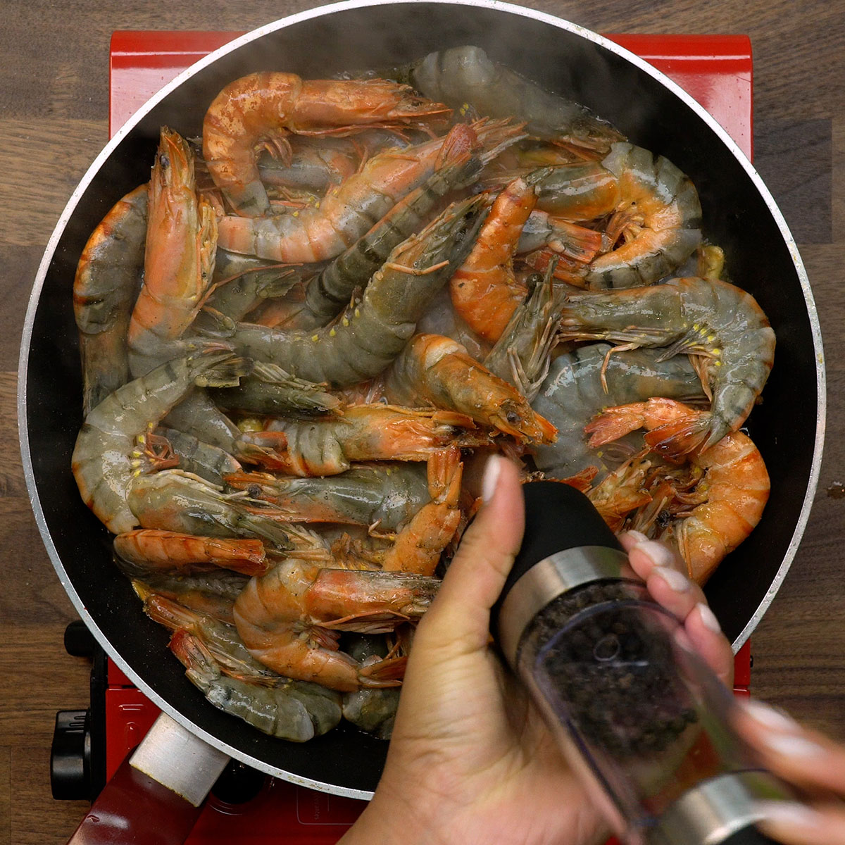Camarão sendo temperado com pimenta-do-reino e sal durante o preparo.