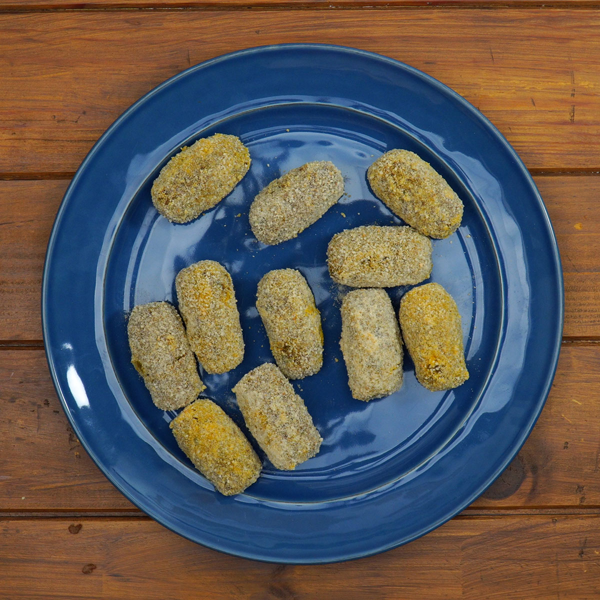 Croquetes sendo passados no ovo batido e na farinha de rosca.