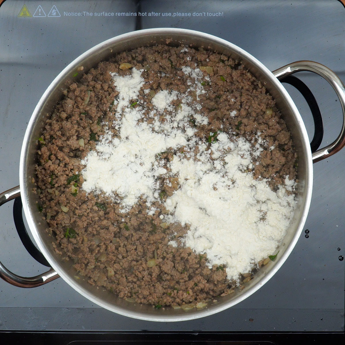 Carne moída sendo temperada com ervas frescas e pimenta-do-reino.