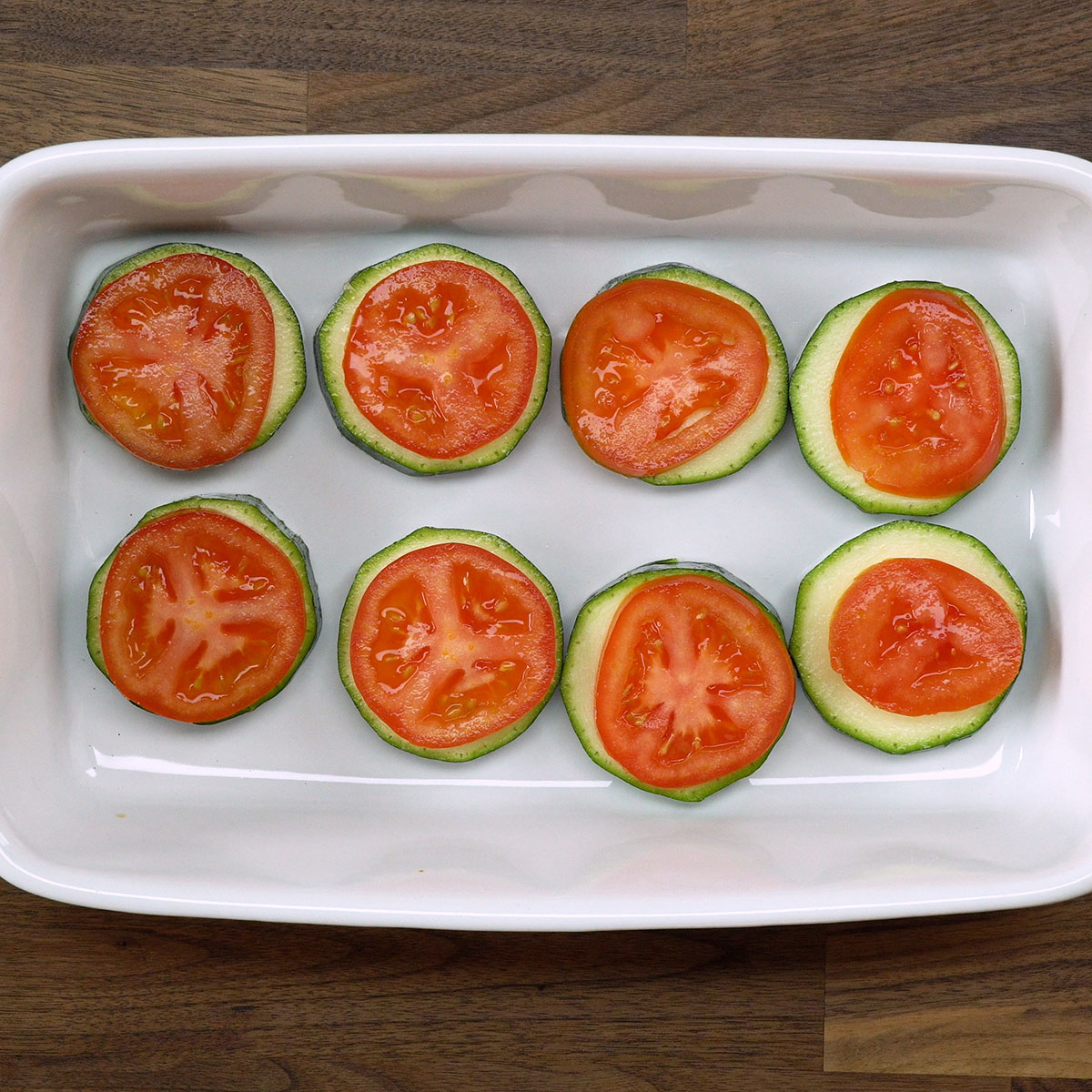 Rodelas de tomate posicionadas sobre a abobrinha em um refratário.