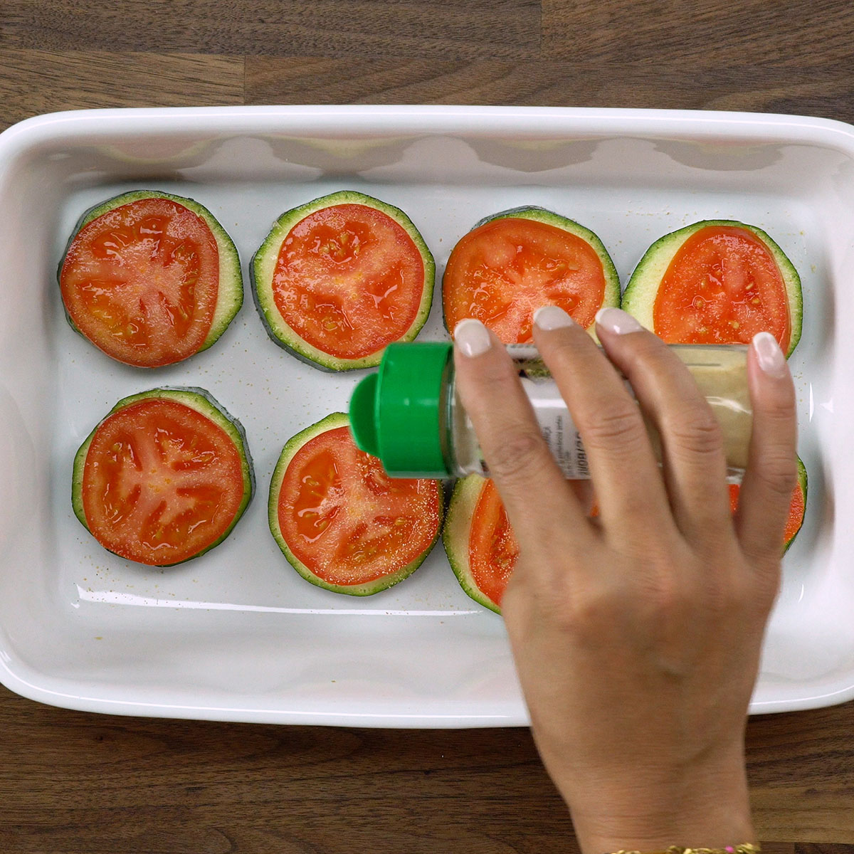 Tomates sobre abobrinha sendo temperados com alho em pó.
