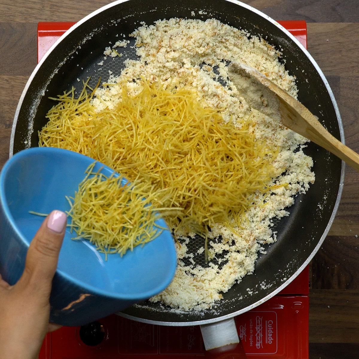 Batata palha sendo misturada à farofa de cebola.