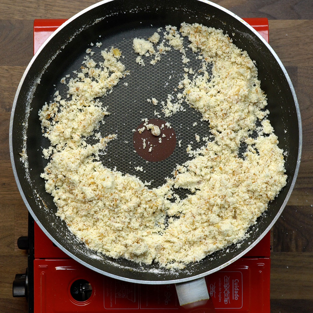 Farofa de mandioca sendo mexida na frigideira para ficar crocante.