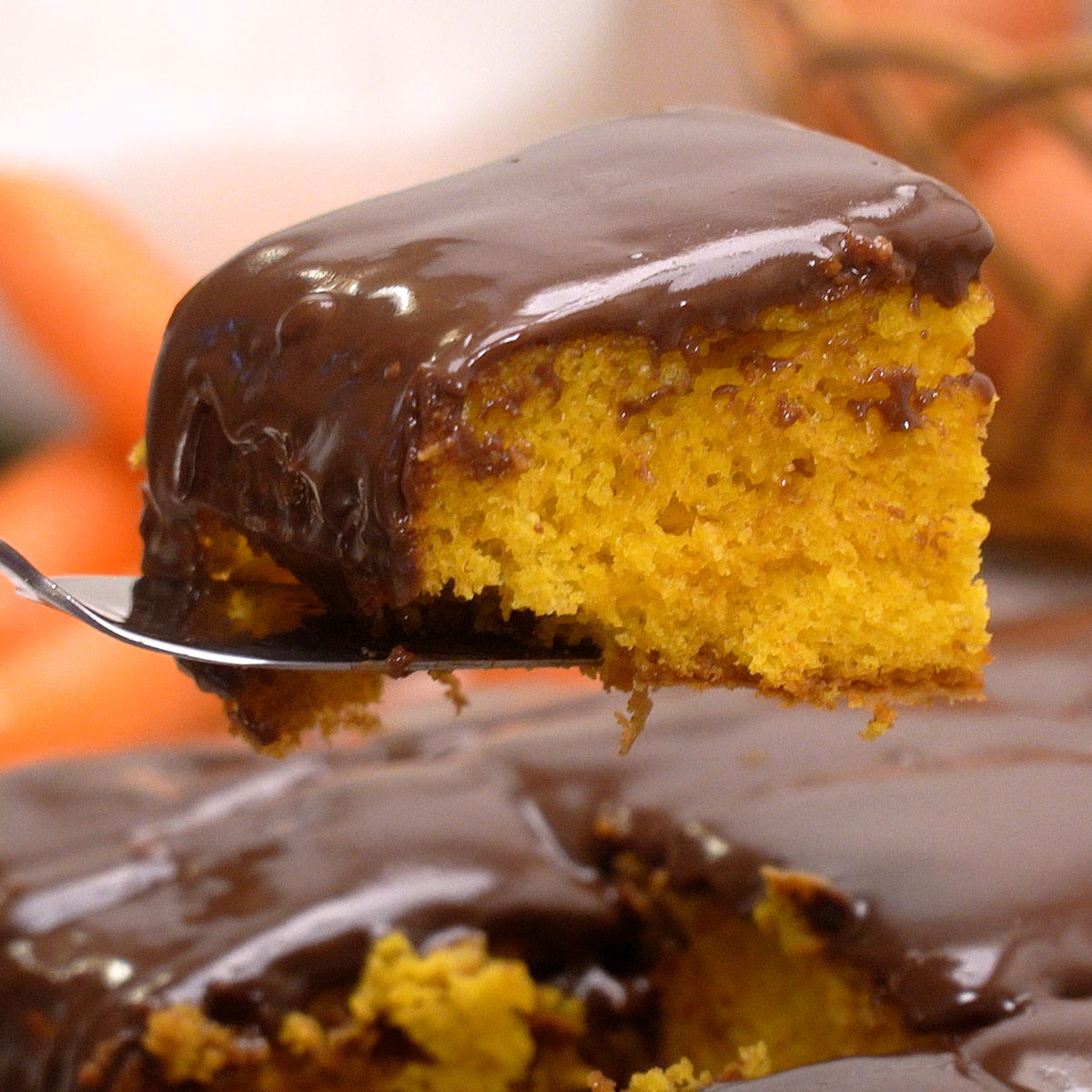 Fatias de bolo de cenoura com cobertura de chocolate sendo servidas.