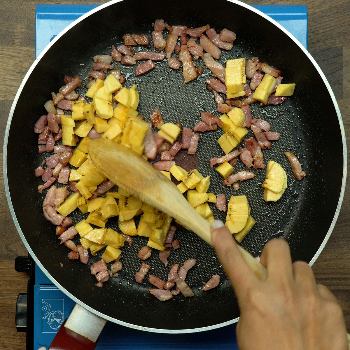 Banana-da-terra sendo adicionada ao bacon e à cebola na frigideira.