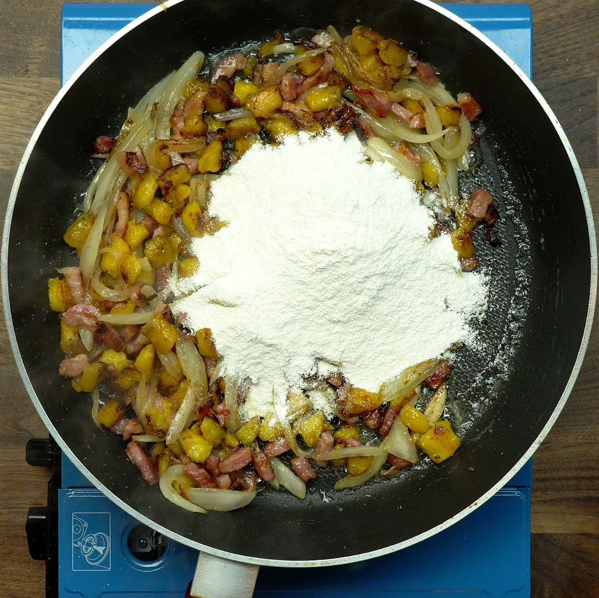 Farinha de mandioca sendo misturada ao bacon e à banana-da-terra na frigideira.