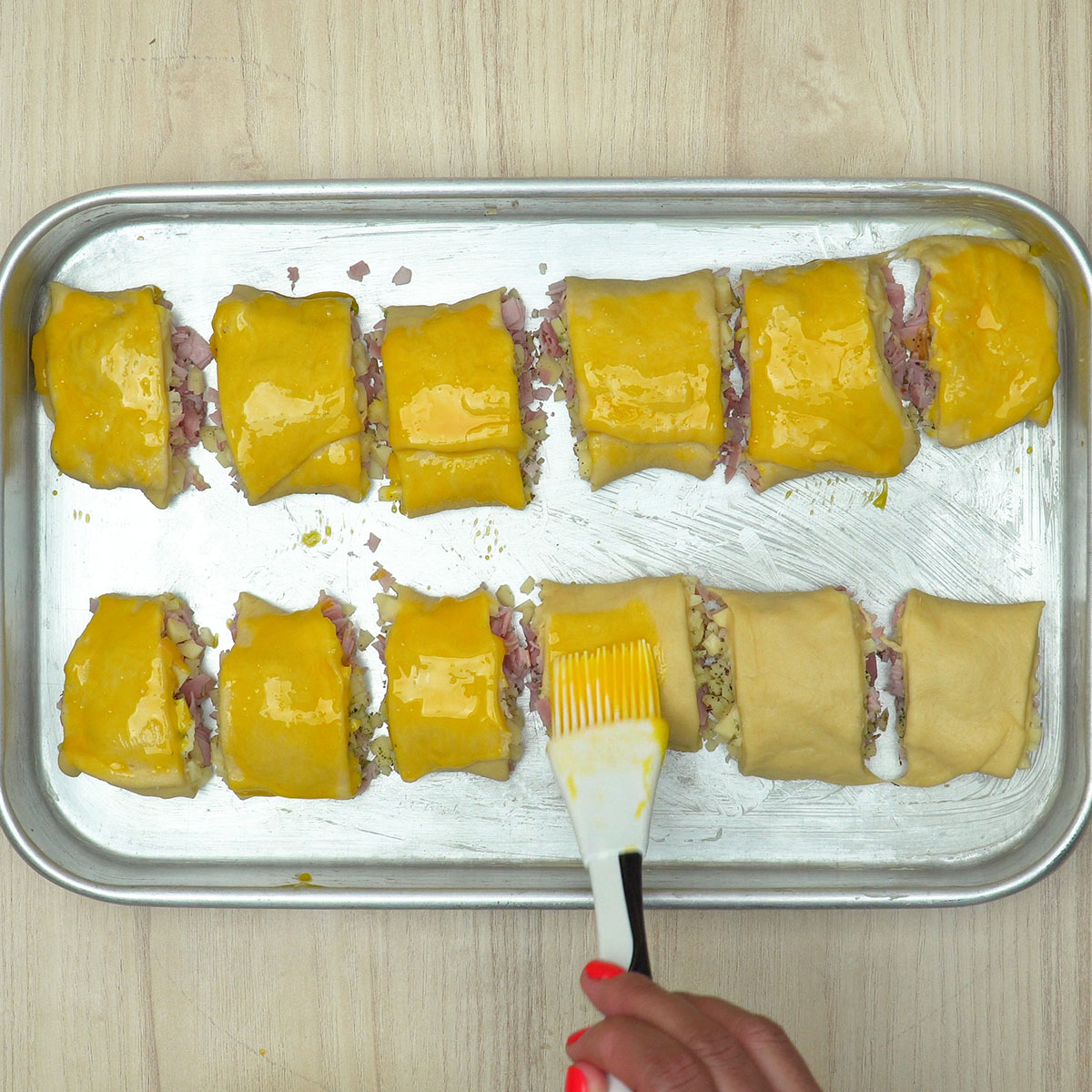 Enroladinhos de presunto e queijo sendo levados ao forno para assar.