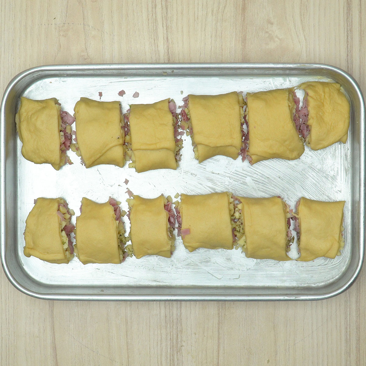 Enroladinhos de presunto e queijo modelados e colocados na forma.