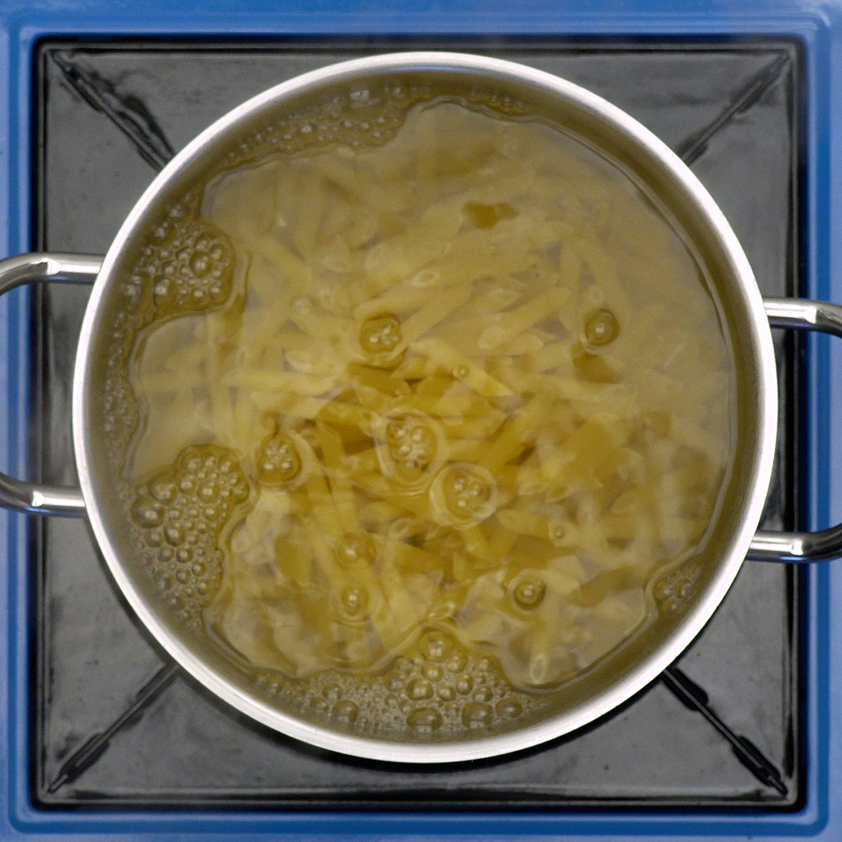 Macarrão penne sendo cozido em panela com água fervente.