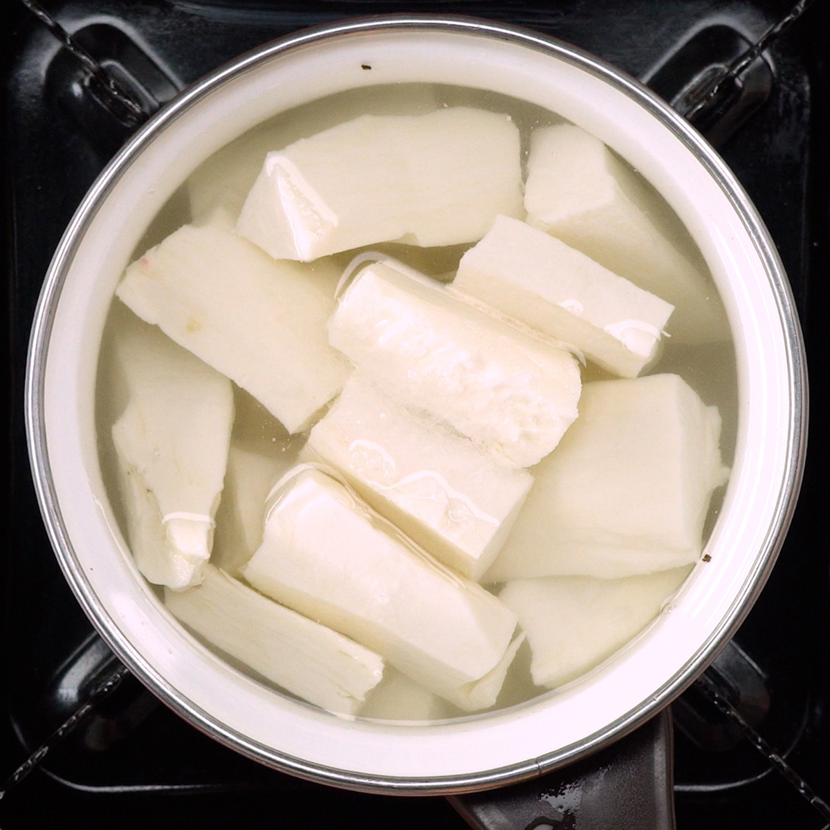 Mandioca cozinhando em panela com água até ficar macia.