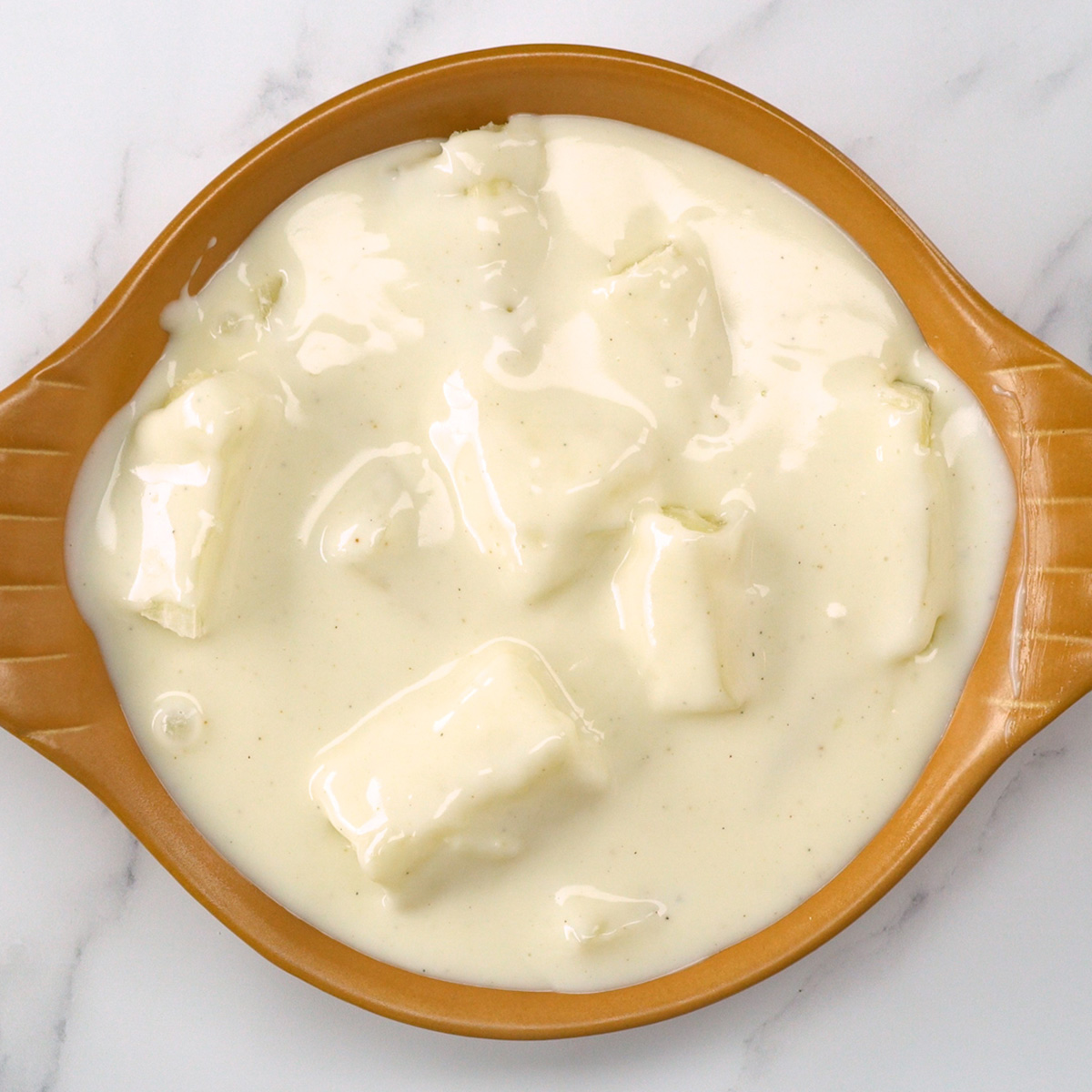 Mandioca coberta com molho branco em um refratário.