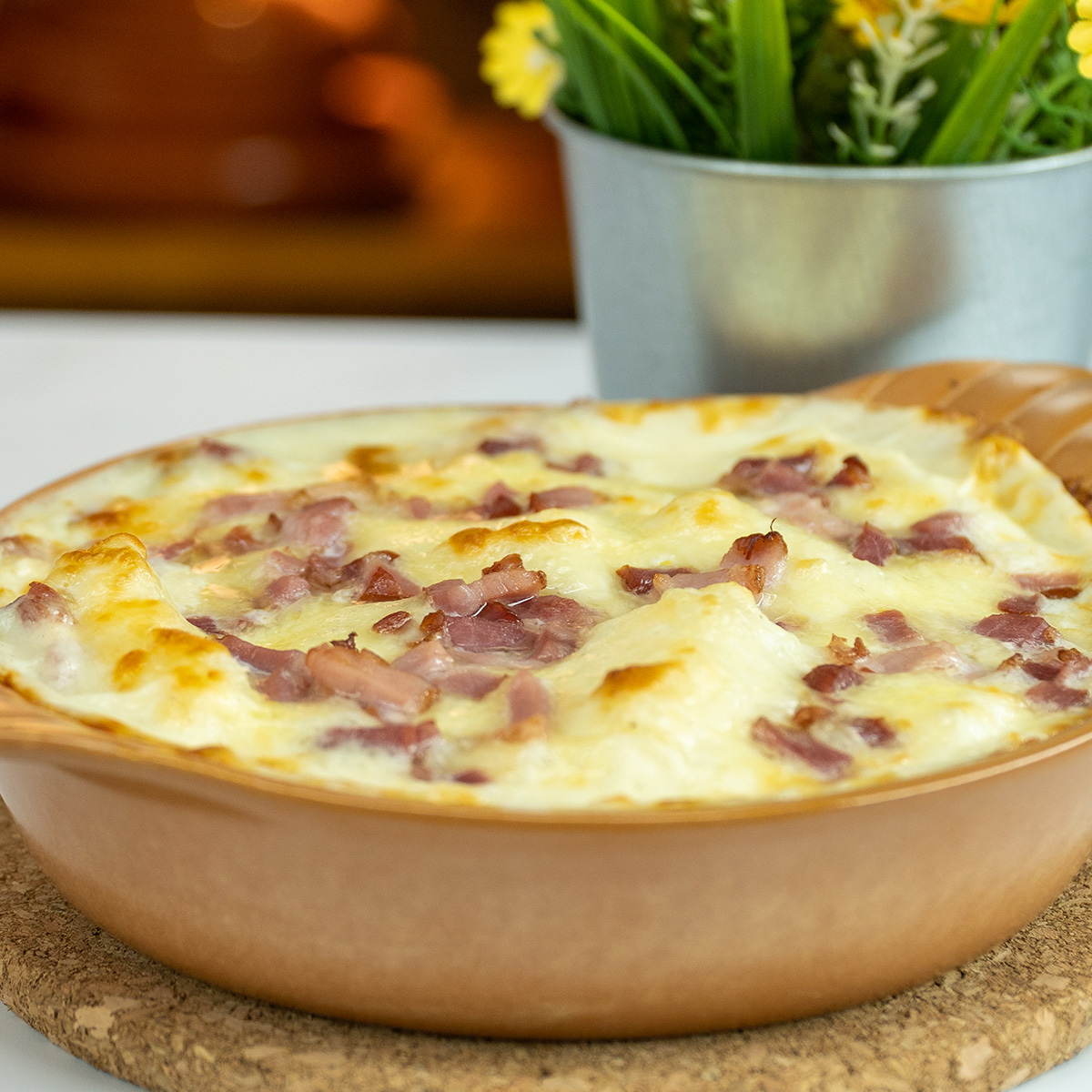 Mandioca de forno gratinada com bacon e molho branco saindo do forno, pronta para servir.