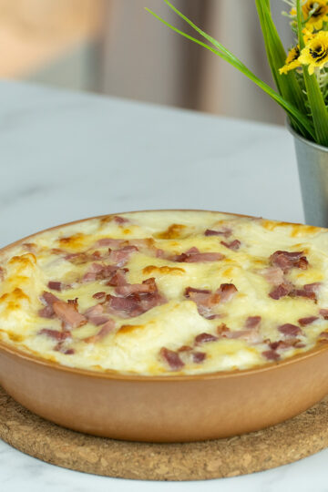 Mandioca de forno gratinada com bacon saindo do forno pronto para ser servido.