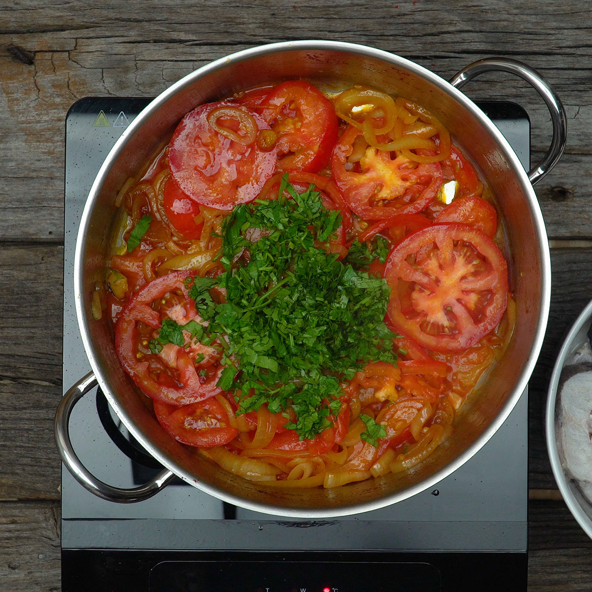 Coentro fresco picado sendo distribuído sobre a base da moqueca.