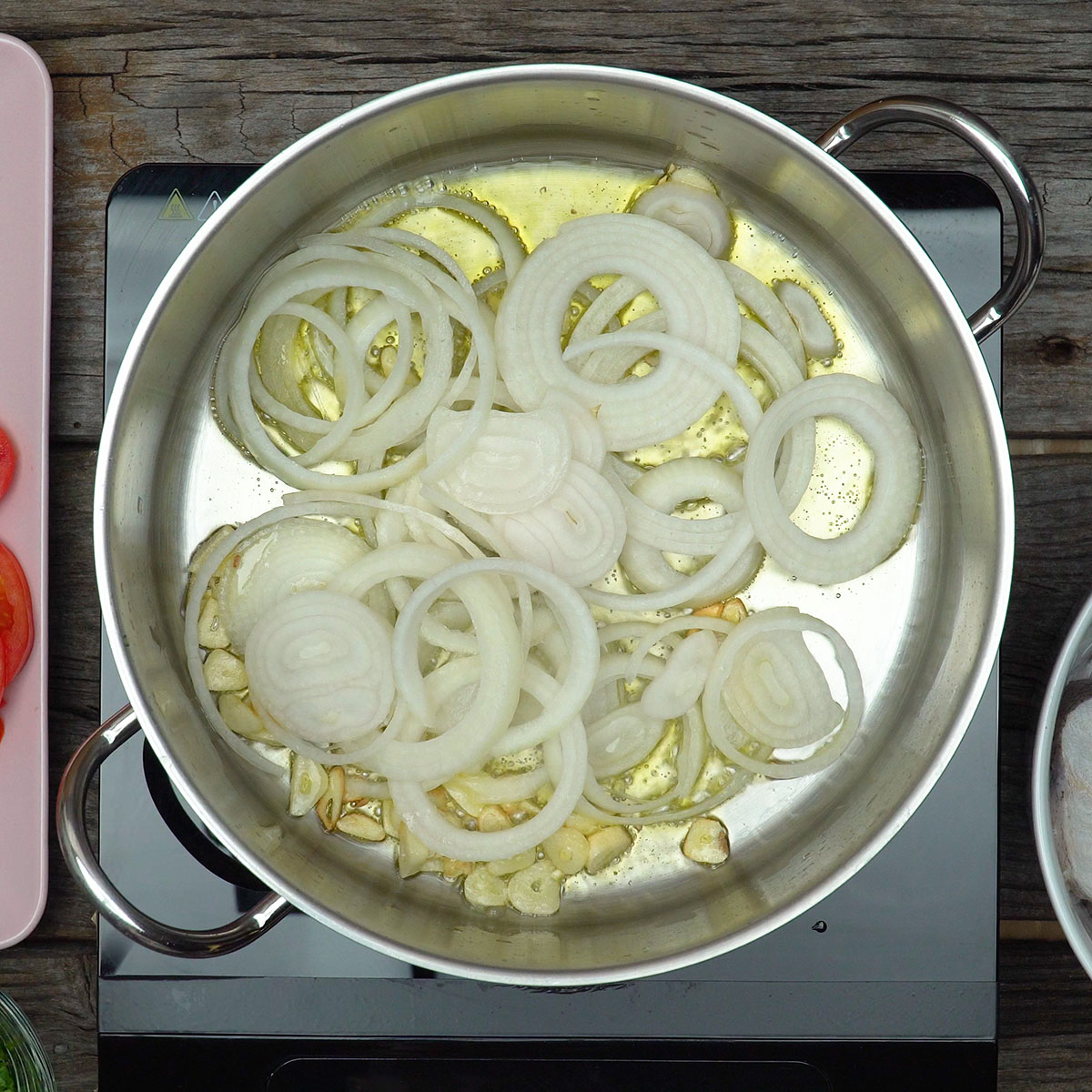 Alho laminado e cebola em rodelas refogando no azeite em uma panela larga.