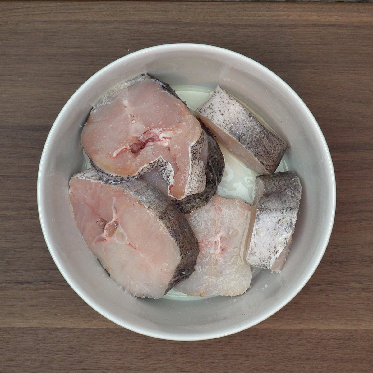 Postas de pescada sendo temperadas com sal e suco de limão.