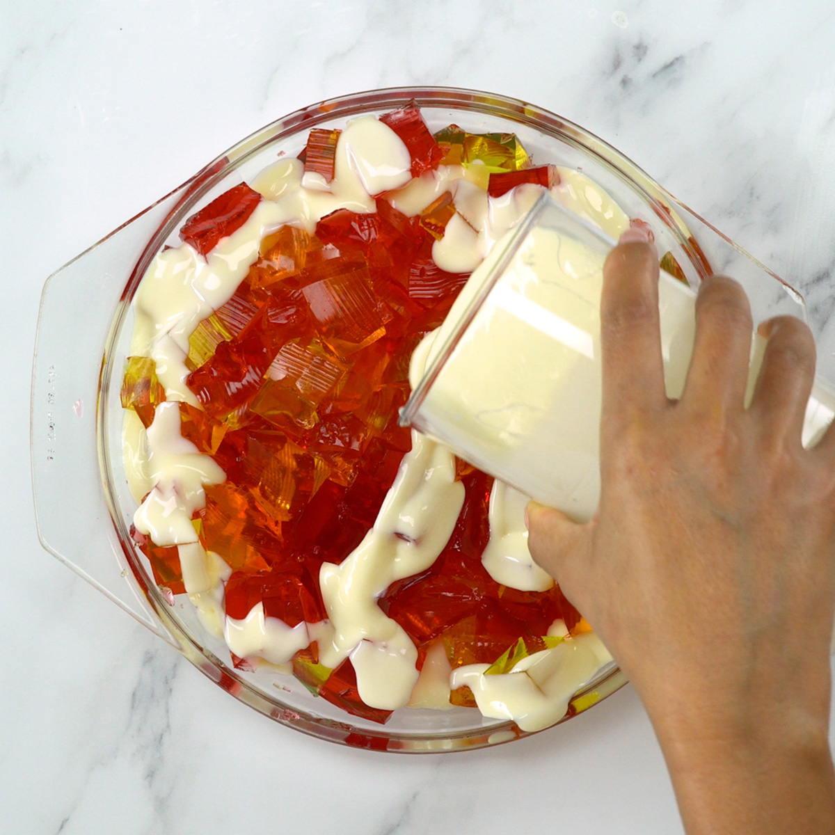 Montagem da gelatina colorida com cubos e creme em refratário.