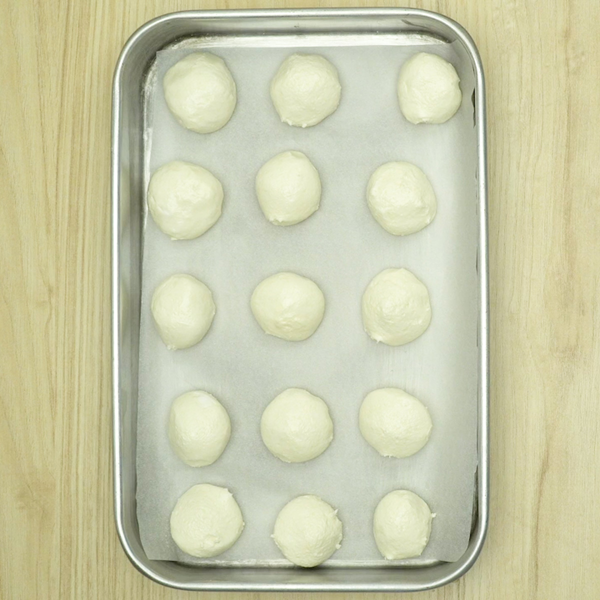 Bolinhas de pão de queijo com tapioca organizadas na assadeira com espaço entre elas.